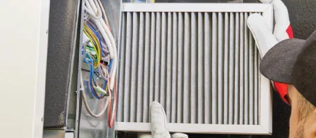 A Reliable Comfort Services technician slides a fresh pleated filter back into a home's furnace, helping keep the indoor air clean and easy to breathe.