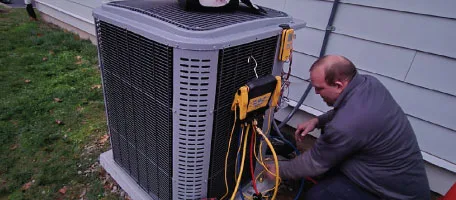 A Reliable Comfort Services technician kneels beside a home's outdoor unit, checking the refrigerant pressures during a heating and cooling tune-up.